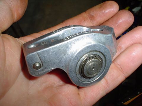 1984 Ford Bronco - A close-up of a metal rocker arm assembly, likely for an engine, held in a person's hand.