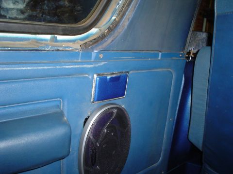 1984 Ford Bronco - Interior close-up of a blue vinyl side panel in a truck cab, with an aftermarket coaxial speaker mounted in a silver grille below a chrome-…