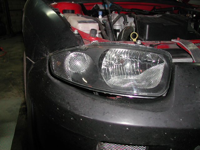 Front corner of a charcoal coupe with hood up, clear headlight, red inner fender