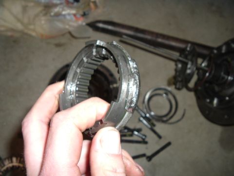 1999 Jeep Grand Cherokee - A damaged transmission synchronizer ring is held up for inspection, with other parts scattered in the background.