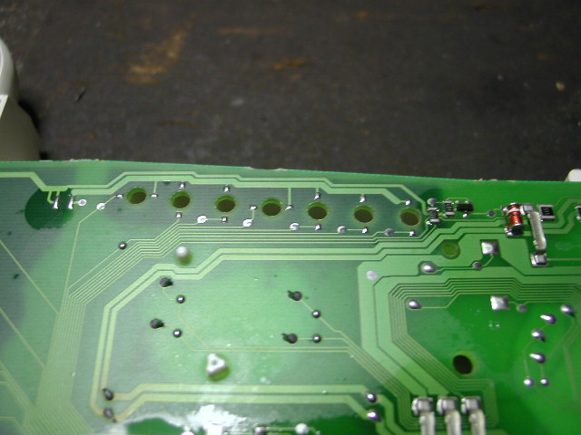 Solder side of green PCB with row of holes, solder joints, and a diode.