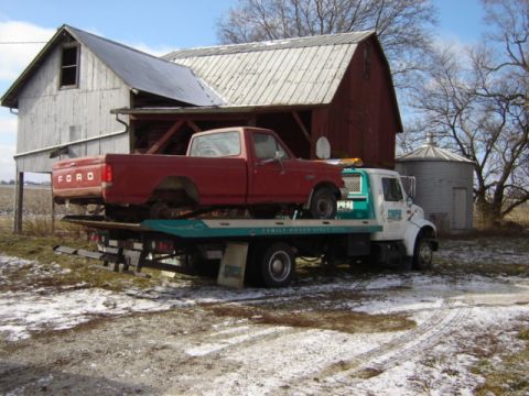 1992 Ford Bronco - A tow truck transports a red Ford pickup truck in front of a barn and silo.