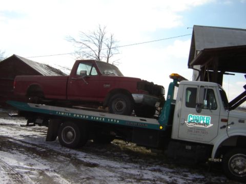 1992 Ford Bronco - A red pickup truck is loaded onto a tow truck, with farm buildings in the background.