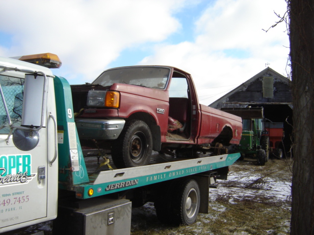 Red 1992 Ford F-350 pickup truck on a tow truck, front 3/4 view, doors open, some damage