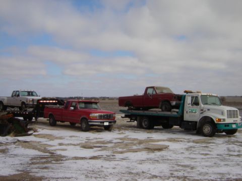 1992 Ford Bronco - A tow truck transports a red pickup, with other trucks visible in the snowy landscape.