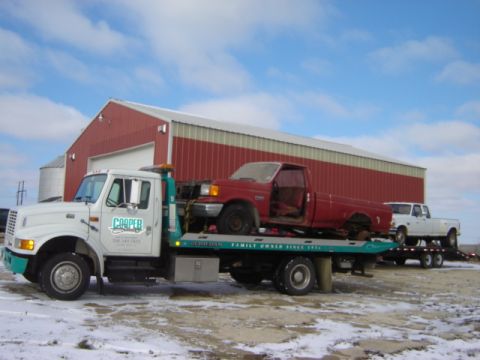 1992 Ford Bronco - Tow truck transports two pickup trucks past a red barn on a snowy day.