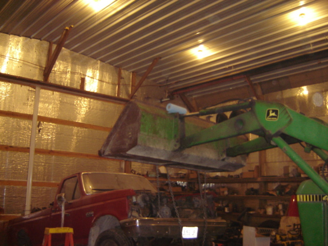 Red pickup truck with front end removed, parked inside a barn