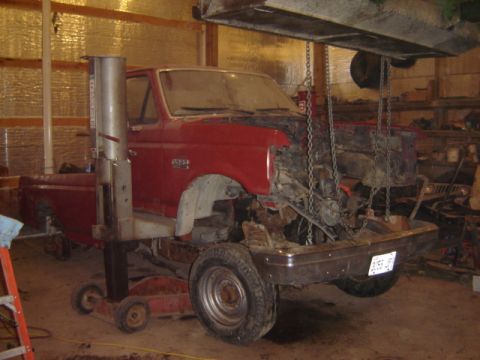 1992 Ford Bronco - This red pickup truck is undergoing repairs in a garage, with its engine compartment disassembled.