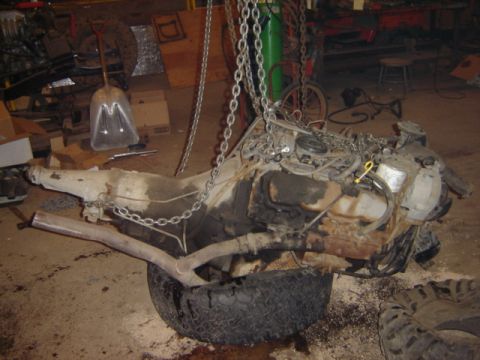 1992 Ford Bronco - An engine and transmission assembly is suspended by chains, with a tire underneath it.