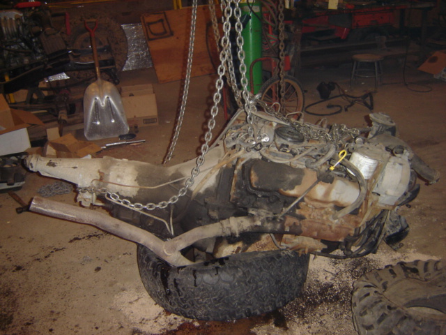 engine and transmission hanging from chains, resting on a tire