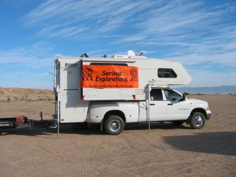 1997 Ford Ranger - A white pickup truck is parked in a desert landscape with a camper shell and an orange banner.