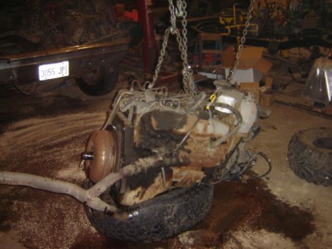 1992 Ford Bronco - Engine assembly suspended by chains, resting on a tire, with a vehicle frame and license plate visible in the background.
