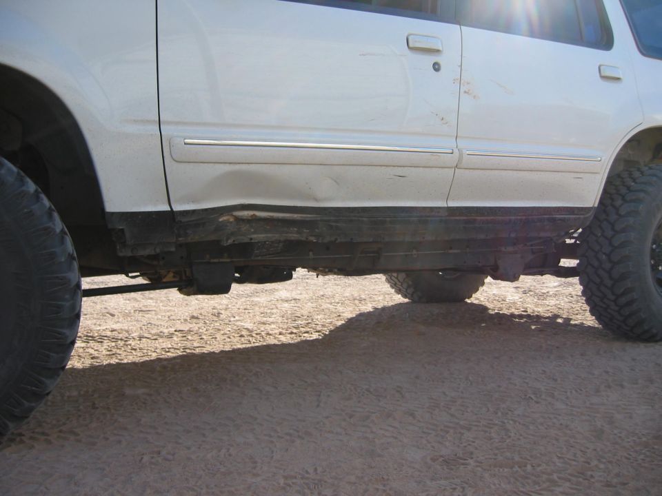 White SUV side with dented rocker panel and large off-road tires