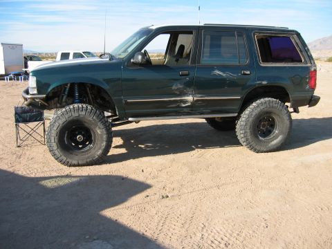 1997 Ford Ranger - Modified SUV with large tires and suspension lift sits on sandy terrain under a clear sky.