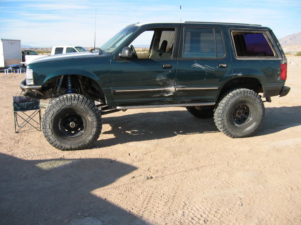 Lifted dark green Ford Explorer on mud tires with tube bumper, side view in the desert