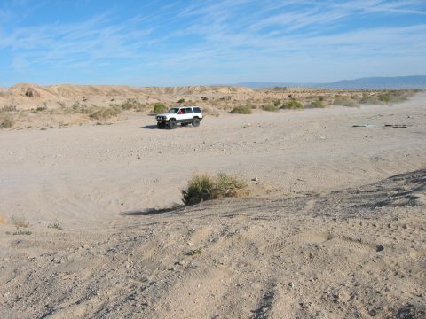 1997 Ford Ranger - A white SUV kicks up dust as it drives through a barren, desert terrain under a clear blue sky.