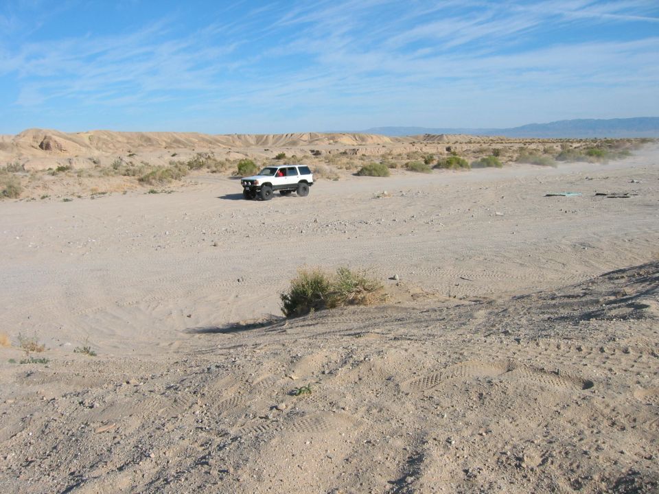 White SUV driving on a dirt road in a desert landscape