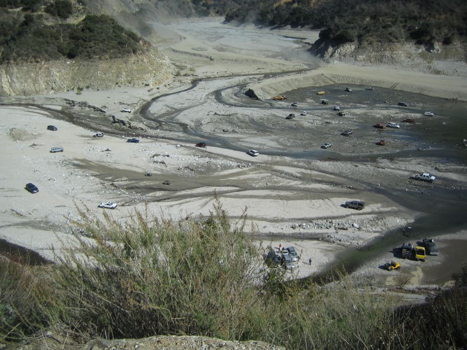 many cars and trucks scattered in a dry, dusty riverbed with a winding path
