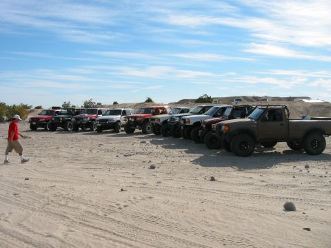 1997 Ford Ranger - A group of modified trucks are lined up in a desert landscape under a blue sky.