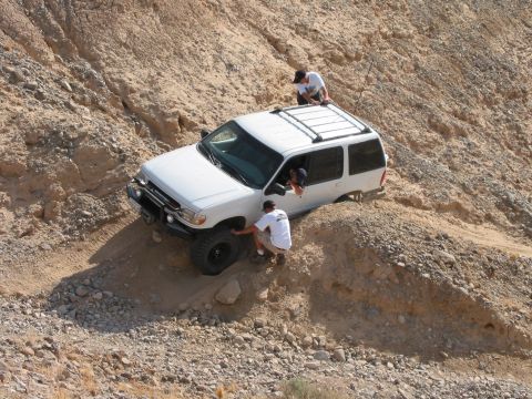 1997 Ford Ranger - Two people are assisting a white SUV that is stuck on a steep, rocky incline.