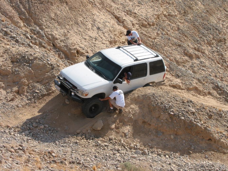 White SUV stuck on a steep dirt hill with two people trying to help it