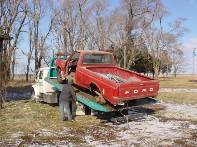 Red Ford pickup truck on a tow truck, rear view. The truck appears to be from the early 1980s