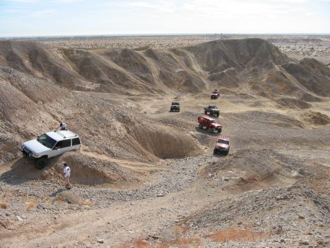 1997 Ford Ranger - Wide overlook of a group of lifted 4x4s strung out along a badlands wash trail, with a white lifted SUV wearing a roof rack parked on the l…