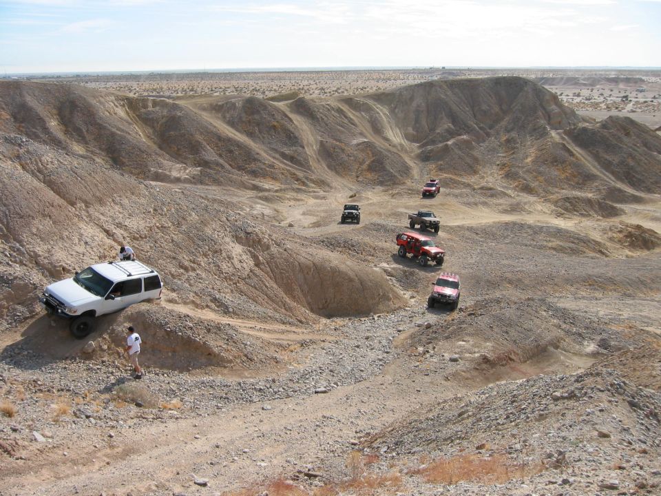 Group of lifted 4x4s spread across a desert badlands trail