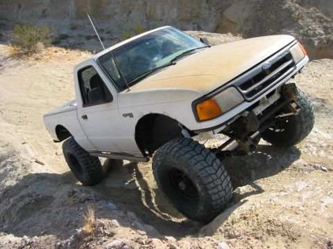 1997 Ford Ranger - Dusty white Ford Ranger 4x4 regular-cab short-bed pickup flexing on a rocky desert trail, three-quarter front view showing a solid-axle-sty…