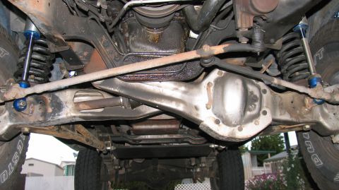 1984 Ford Bronco - The underside of a vehicle reveals its front axle, steering linkage, and suspension system.