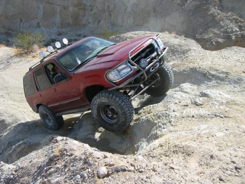 1997 Ford Ranger - Elevated three-quarter front view of a lifted maroon two-door Ford Explorer Sport crawling down an eroded rock ledge, front tire drooped in…