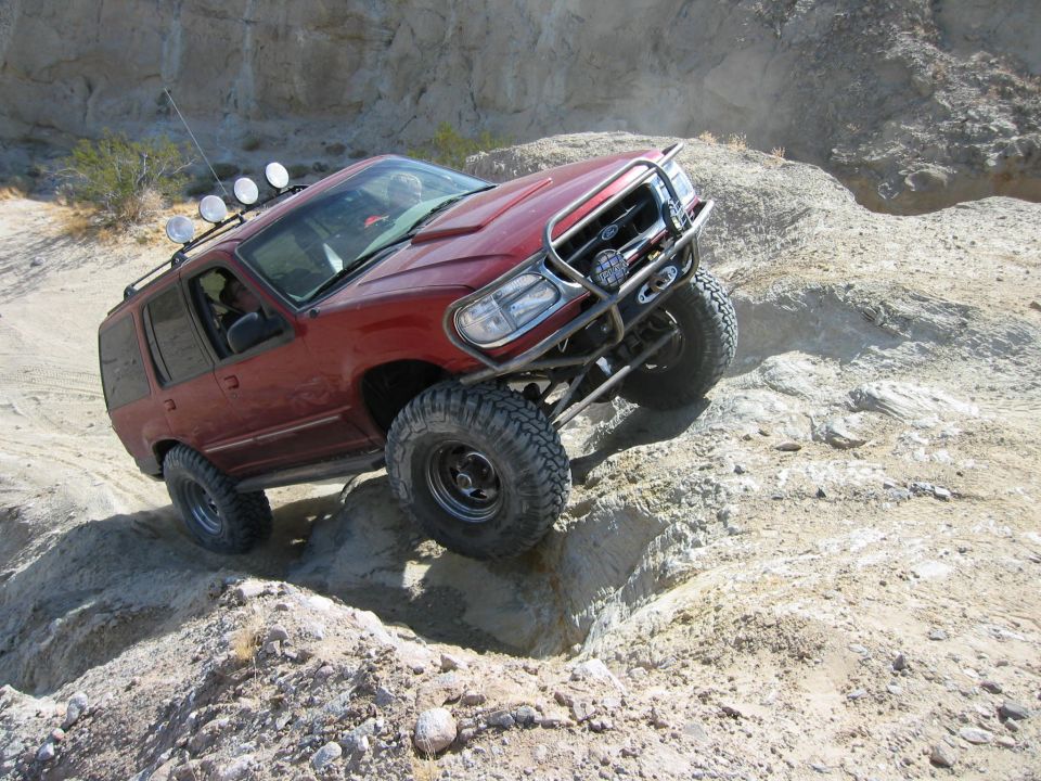 Lifted maroon Ford Explorer Sport with tube bumper and winch crawling down a rock ledge