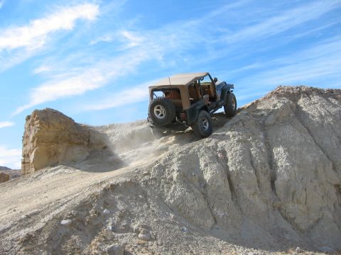 1997 Ford Ranger - A dark Jeep Wrangler with a tan soft top and tan interior crests a steep, eroded chalky ridge, kicking up dust from its rear tires against…