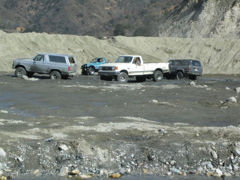 Four-wheel drive vehicles navigating a muddy off-road course with hills in the background
