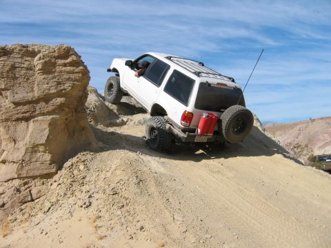 1997 Ford Ranger - A white SUV navigates a steep, sandy hill with a rocky outcrop to its left.