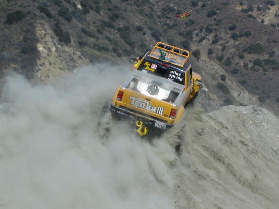 Yellow pickup truck with "Tonka III" on tailgate driving down a dusty hill
