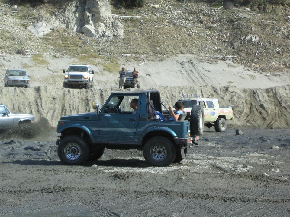 Teal 1987 Suzuki Samurai with spare tire on rear, driving off-road