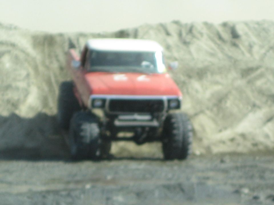 Red pickup truck with white roof and large off-road tires, angled front view