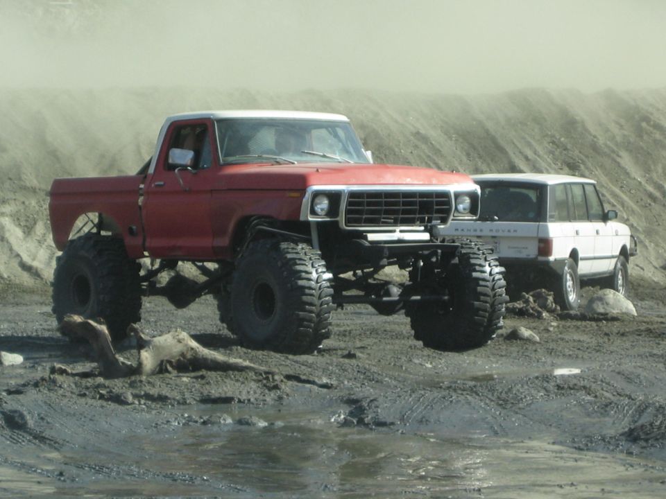 Red lifted pickup truck with large tires, front view. White Range Rover in background