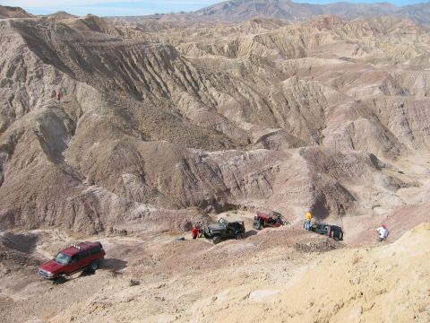 1997 Ford Ranger - Overhead view of a four-wheel-drive group parked along a narrow ledge trail cut into eroded purple-and-tan badlands, with a red Ford Explor…