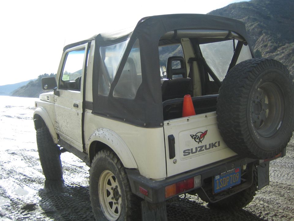 White 1987 Suzuki Samurai soft top with spare tire on rear, parked on beach