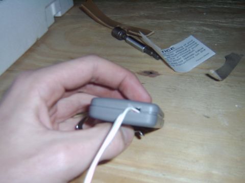1998 Jeep TJ - Hand holding a gray electronic device with a white wire, with a screwdriver and instructions nearby.