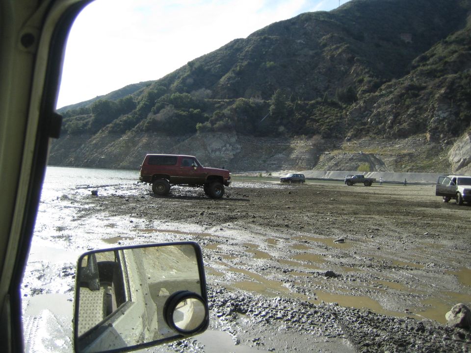 Red SUV with lifted suspension on muddy shore, other vehicles in background