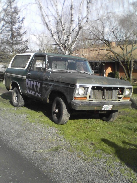 1978 Ford Bronco with "Dirty Deeds" painted on the side, parked on gravel and grass