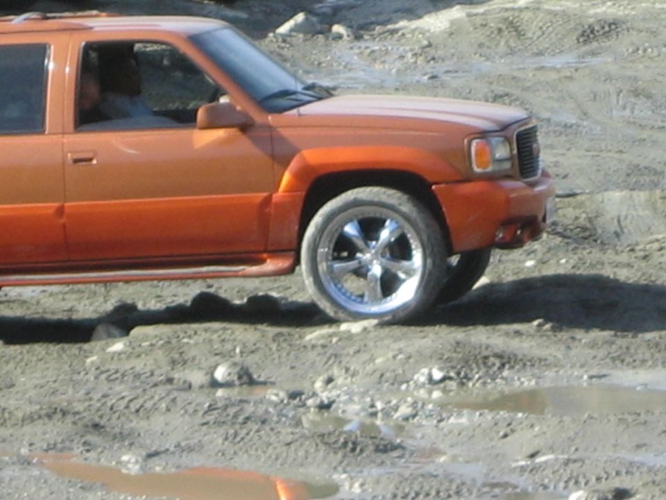 Orange SUV with chrome rims on muddy terrain