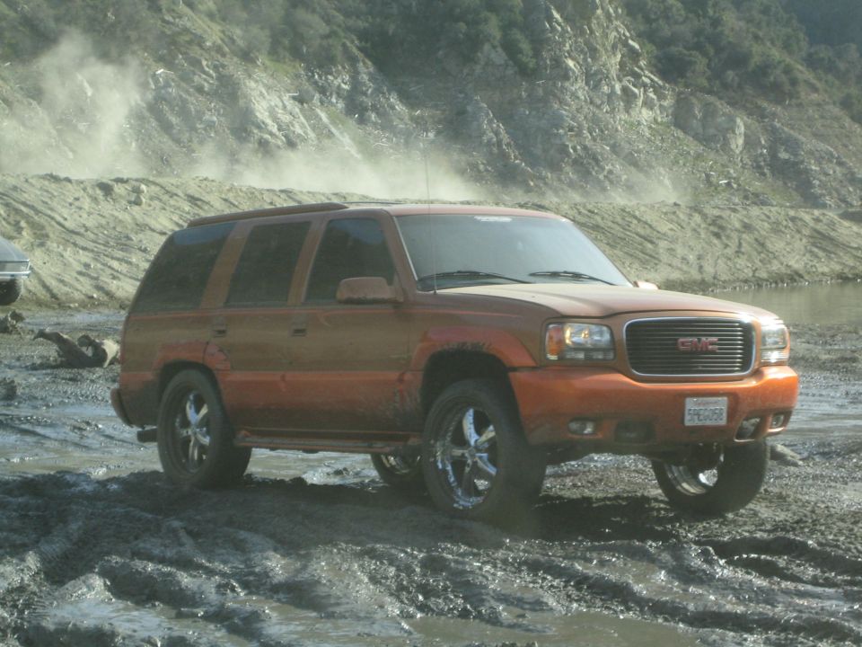 Orange GMC SUV with chrome wheels stuck in mud, front grille visible