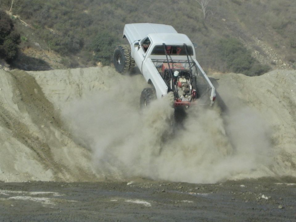 White pickup truck with large tires kicking up dust on a dirt hill