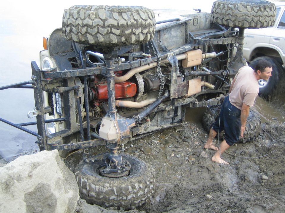 Overturned 1987 Suzuki Samurai in mud, with a man nearby and another vehicle in the background