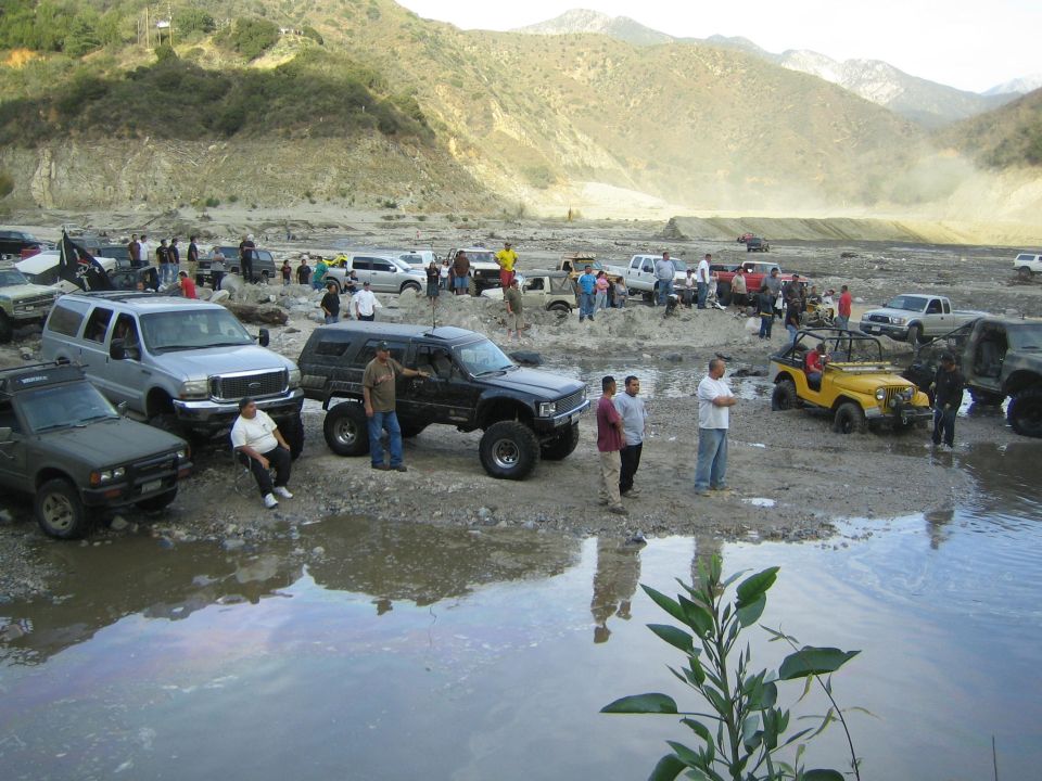Off-road vehicles gathered in a dry riverbed with people