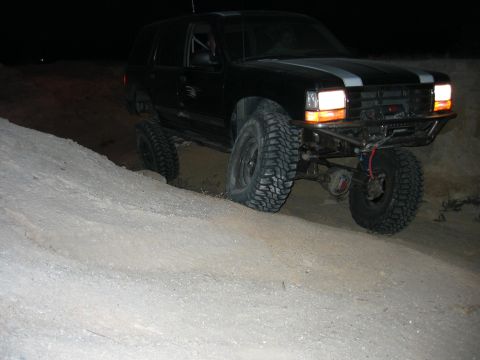1997 Ford Ranger - Modified SUV with off-road tires climbs a dirt hill at night, showing custom bumper and racing stripes.